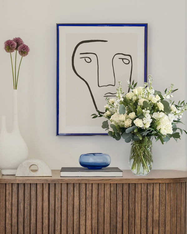 Elegant white floral arrangement with roses and greenery in a glass vase, styled in a modern interior setting. Perfect for weddings, sympathy gifts, and luxury home dƩcor.
