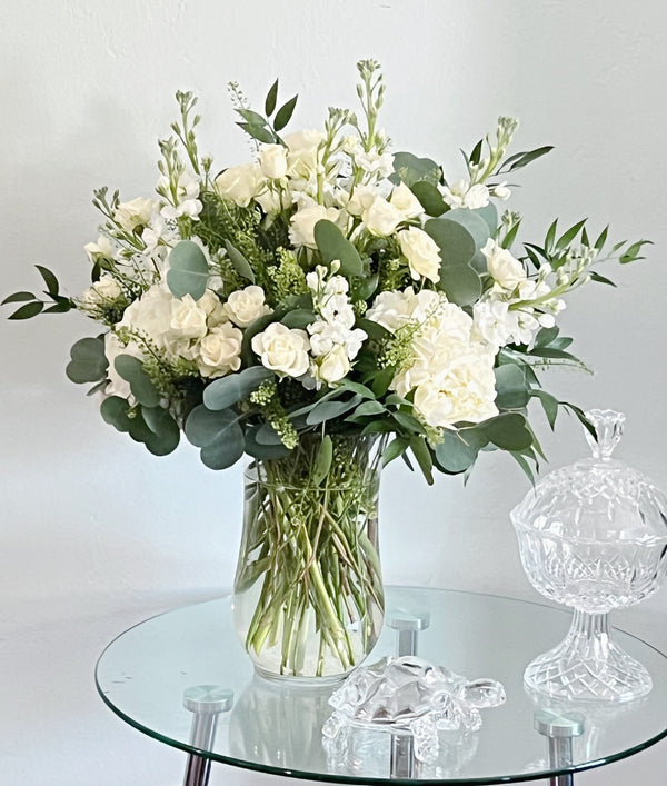 White roses and fresh greenery in a chic glass vase, a timeless floral gift for weddings, birthdays, and special occasions.